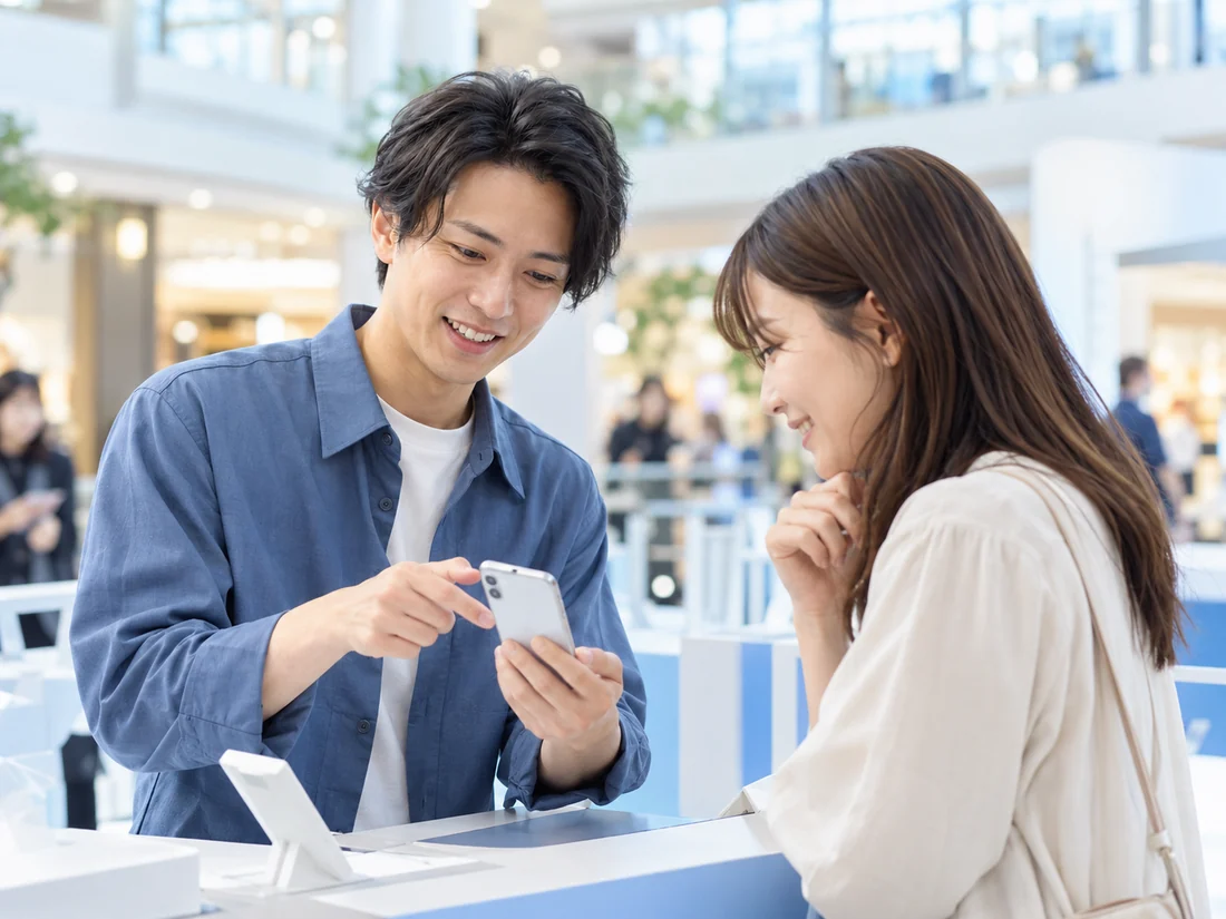 お客様とスマートフォンを見ながら案内する架空の成人スタッフ